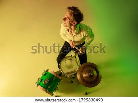 Young musician, drummer in neon in studio