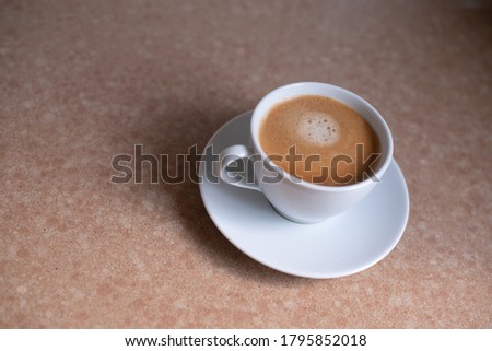white cup of coffee on the table with small saucer. cup pair with aromatic expresso. top side. brown background table. one glass.