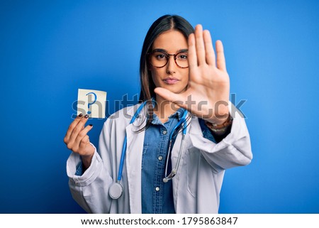 Young beautiful brunette doctor woman holding paper with question mark symbol message with open hand doing stop sign with serious and confident expression, defense gesture