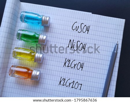 Colored solutions in glass reagent bottles - copper sulfate blue, nickel sulfate green, potassium chromate yellow and potassium dichromate orange. Transition metal compounds with chemical formulas.