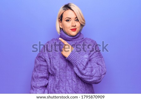 Beautiful blonde plus size woman wearing casual turtleneck sweater over purple background Pointing with hand finger to the side showing advertisement, serious and calm face