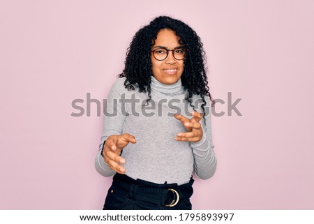 Young african american woman wearing turtleneck sweater and glasses over pink background disgusted expression, displeased and fearful doing disgust face because aversion reaction.