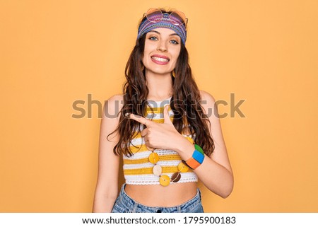Young beautiful hippie woman with blue eyes wearing accesories and sunnglasses cheerful with a smile on face pointing with hand and finger up to the side with happy and natural expression