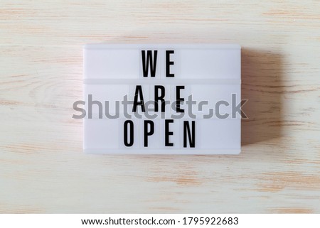 Signboard WE ARE OPEN of lightbox on wood background. Open sign hanging on vintage wooden wall. Opening sign of cafe, bar, or restaurant. Business open and welcome. Concept of quarantine mitigation