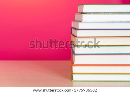 Stack of colorful books, bright colorful pink background, free copy space. Books on table, no labels, blank spine. Back to school. Education background.
