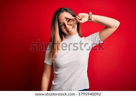 Beautiful blonde woman with blue eyes wearing casual white t-shirt over red background Doing peace symbol with fingers over face, smiling cheerful showing victory