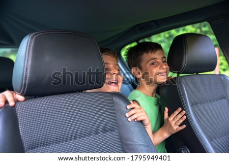 Two boys are sitting in the back seat of the car and having fun