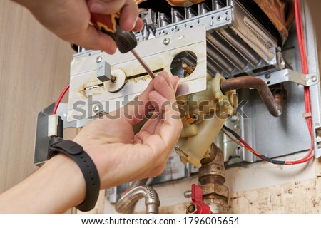 service technician repairing gas water heater indoors. water heater maintenance. diy concept. Royalty-Free Stock Photo #1796005654