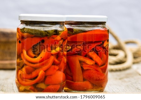 Glass jars with pickled red bell peppers.Preserved food concept, canned vegetables isolated in a rustic composition. Royalty-Free Stock Photo #1796009065
