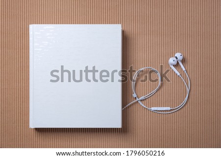 White headphones and a white book on the blue and beige background. Audio book reading online.