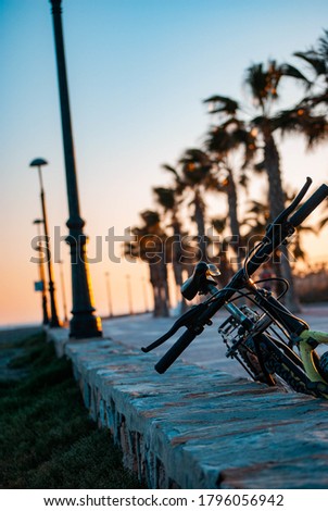 A vertical shot of a bicycle parked on the street with the sunset in the background