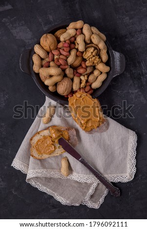 Peanut butter on bread, peanut sandwich, nuts
scattered across the table on a plate. Dark background. Copy Space for Your Text Vertically