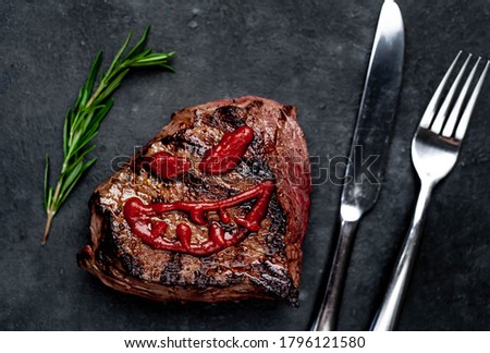 grilled beef steak with spices, knife and fork for halloween on stone background