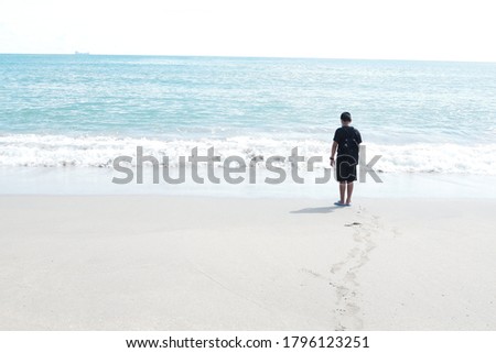 Beautiful seascape a boy wearing a black shirt with jeans was relaxing on the white sand beach. In front of him is a bright blue sea. Small grained sand and blue sky background.