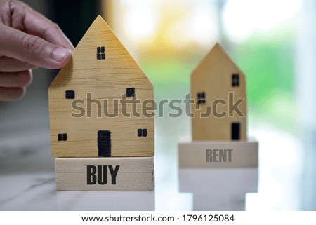 Businessman choosing mini wood house model with word BUY, Choose what's the best,financial concept for buy house or loan for plan business investment of real estate concept.background copy space.
