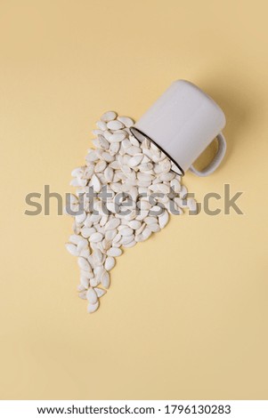 White pumpkin seeds scattered from a mug on a colored background. Image contains space for text