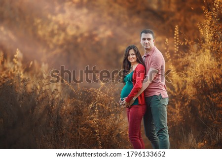 Pregnant woman with husband in the autumn forest. Mother and father. Happy parents. Autumn family portrait. Pregnancy, maternity, expectation concept. Beautiful tender mood photo of pregnancy.