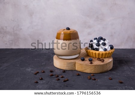  Dalgona coffee, airy creamy whipped coffee on a dark background. Cake with cream and berries. Space for text with copy space