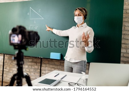 Elementary school teacher pointing at chalkboard while teaching mathematic online during COIVD-19 epidemic.  Royalty-Free Stock Photo #1796164552