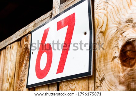 A plaque with the number 67 hangs on a wooden surface. Close-up, selective shot.
