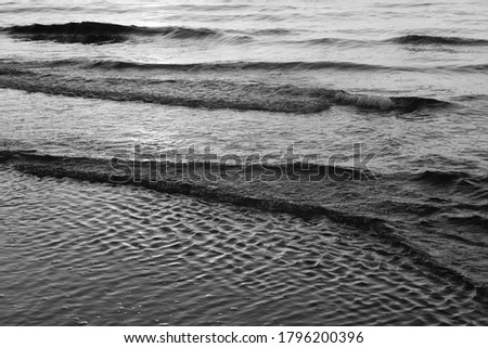 Black & White background depicting small waves arriving at the coast of an ocean