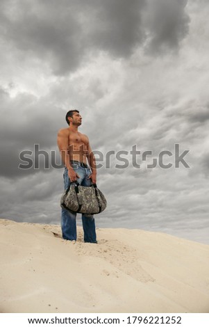 Muscular young man with sand bag in desert. Fitness training workout concept.