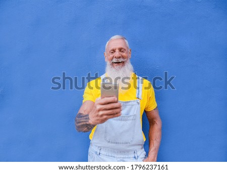Elderly hipster man with mobile phone enjoy technology - Trendy senior man laughing