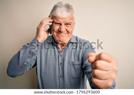 Senior hoary man having conversation talking on the smartphone over white background annoyed and frustrated shouting with anger, crazy and yelling with raised hand, anger concept