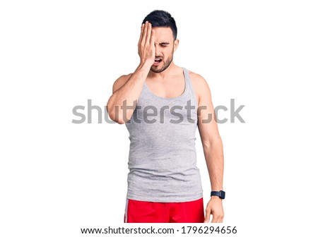 Young handsome man wearing swimwear and sleeveless t-shirt yawning tired covering half face, eye and mouth with hand. face hurts in pain. 
