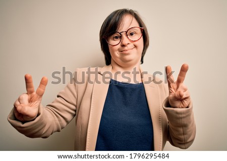 Young down syndrome business woman wearing glasses standing over isolated background smiling looking to the camera showing fingers doing victory sign. Number two.