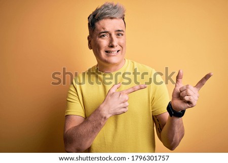 Young handsome modern man wearing yellow shirt over yellow isolated background Pointing aside worried and nervous with both hands, concerned and surprised expression