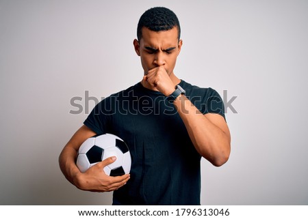 Handsome african american man playing footbal holding soccer ball over white background feeling unwell and coughing as symptom for cold or bronchitis. Health care concept.