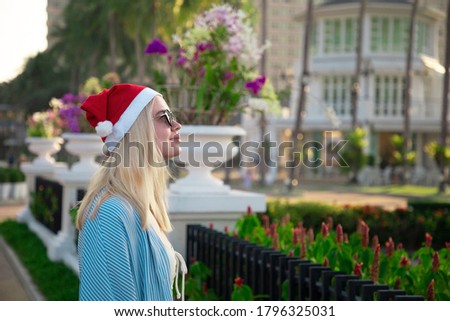 Girl in a red Christmas hat next to the swimming pool with blue water. Holiday concept