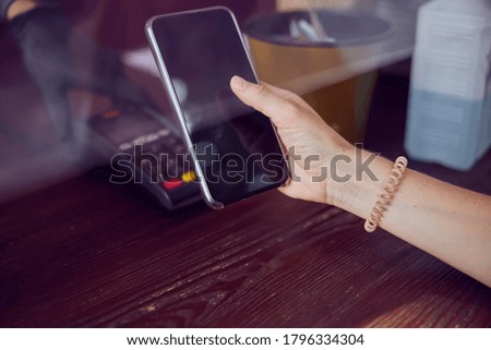 Close-up shot of a hand with a scrunchy of young female who is paying with a smartphone 