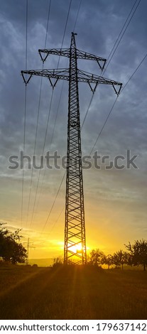 The sun goes down behind a high-voltage tower

