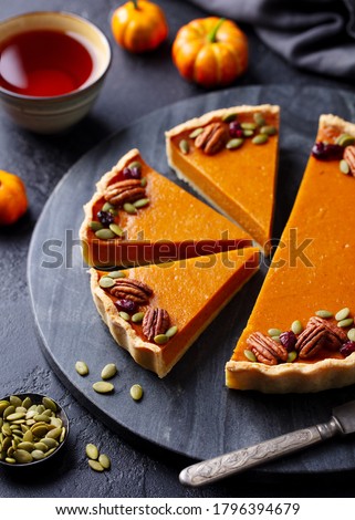 Pumpkin pie on marble board with cup of tea. Grey background.