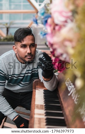 portrait model sitting near a piano which covered with flowers and the model is holding a flower in his hand