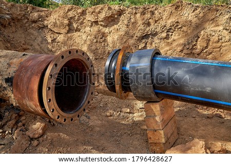 An old steel water pipe with a welded flange lies next to a new plastic pipe installed to connect the water supply system Royalty-Free Stock Photo #1796428627
