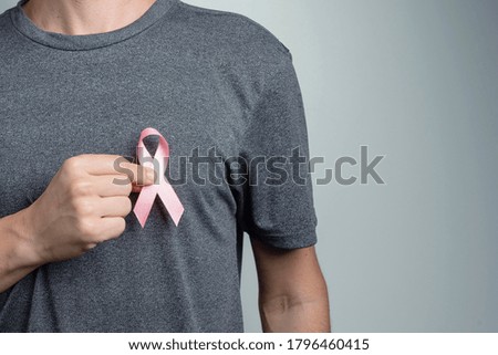 Man putting pink ribbon on his shirt. Awareness symbol.