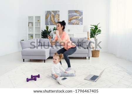 Mom uses smart phone while doing morning work-out at home. Mother does fitness exercises, healthy lifestyle concept. Royalty-Free Stock Photo #1796467405