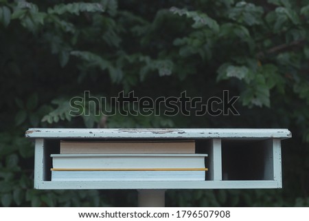 White Vintage Table Outdoors with books on small shelf - blurry green leafy background