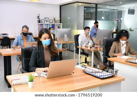 Asian office workers wearing face masks working in new normal office and doing social distancing during corona virus covid-19 pandemic Royalty-Free Stock Photo #1796519200