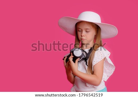 Portrait of a girl traveler, about traveling, holding a camera in her hands in a Studio hat on a pink background