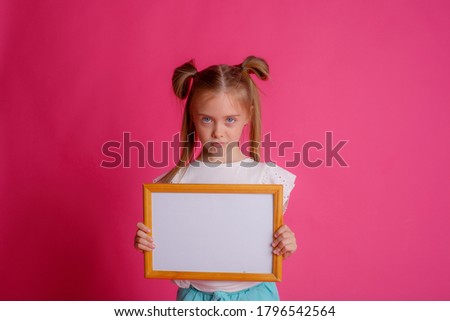 Portrait of a girl holding an empty frame, upset place for text Studio on a pink background