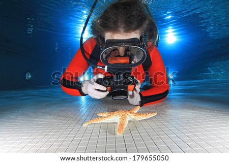 Scuba woman with camera taking pictures of starfish underwater in the pool 