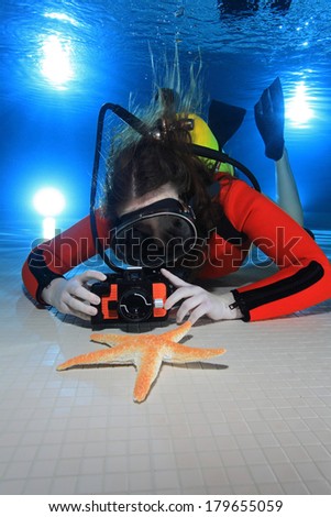 Scuba woman with camera taking pictures of starfish underwater in the pool 