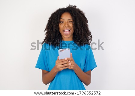 Portrait of Young african woman with curly hair wearing casual blue shirt standing against white background taking a selfie  celebrating success