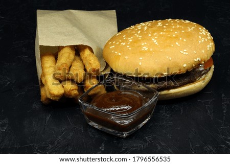 
Chicken sticks in a package, hamburger, tomato sauce on a black background. Side view