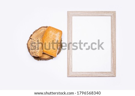 Still life of organic products. Empty wooden frame with space for text. Organic bread stacked on a round piece of wood. Everything is placed on a bright table. Flat, top view, no people.