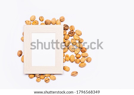 Wooden frame with an empty space for text, lying flat on loosely arranged walnuts. Everything is arranged on a bright table. Flat, top view, no people.